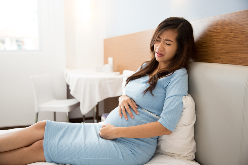 Asian pregnant woman has stomachache sitting on her bed